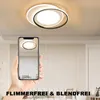A hand holding a smartphone displaying a ceiling light, with the actual ceiling light visible above. The background shows a living room setting. Náhľad obrázku produktu
