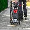 A person is holding a Lehmann Hochdruckreiniger Hudson pressure washer on a paved walkway. Podgląd zdjęcia produktu