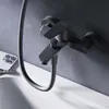 A black bathtub faucet mounted on a dark gray tiled wall, with a white bathtub edge in the foreground and a smartphone on the left. Produktbild-Vorschau