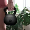 A person holding a black kettlebell in a home gym setting with plants in the background. Náhľad obrázku produktu