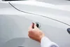 A person's hand is shown using a tool to repair a dent on a white car. Produktbild-Vorschau