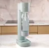 A mint-colored soda maker with a clear bottle filled with water sits on a marble countertop in a kitchen. Produktbild-Vorschau