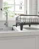 A black dish rack is filled with white dishes and glasses, positioned on a white countertop next to a sink with water flowing from the faucet. Náhled obrázku produktu