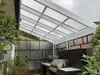 An outdoor patio area with a polycarbonate roof, a built-in counter with a grill, and surrounding greenery. Voir les images du produit