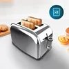 A chrome toaster with two slices of toast in it, placed on a white surface with some baked goods in the background. Anteprima dell’immagine prodotto