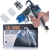 A hand holding a paint sprayer with accessories and packaging in the background. Anteprima dell’immagine prodotto