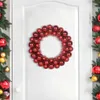 A red Christmas ball wreath is displayed on a white door, with parts of decorated Christmas trees visible on either side. Produktbild-Vorschau