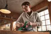 A young person is using a power planer on a piece of wood in a workshop. Produktbild-Vorschau