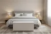 A bedroom scene with a bed, nightstands, lamps, and a storage chest in the foreground. Anteprima dell’immagine prodotto