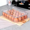 An egg container with a lid filled with eggs, placed on a wooden board on a kitchen counter. Náhled obrázku produktu