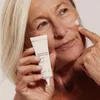 An older woman is applying cream to her face, holding the product tube. Náhľad obrázku produktu