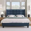 A bedroom scene with a blue upholstered bed as the main focus, set against a backdrop of large windows and subtle wall decor. Produktbild-Vorschau
