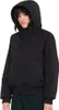 A woman wearing a black hooded jacket and green pants, shown from the chest up against a white background.