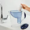 A hand is inserting a filter cartridge into a water filter pitcher next to a kitchen faucet. Anteprima dell’immagine prodotto