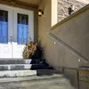 A stainless steel handrail is installed on the exterior wall of a house next to a set of concrete stairs and a double door. Náhled obrázku produktu