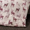 A close-up view of a beige fabric with a repeating pattern of burgundy deer and plaid designs. Produktbild-Vorschau