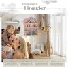 A family with a baby is posing in a nursery decorated with a giraffe plush toy and a wall shelf filled with toys. Produktbild-Vorschau