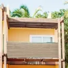 A balcony with a striped privacy screen attached to the railing, surrounded by palm trees and a yellow wall. Podgląd zdjęcia produktu