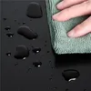 A hand is wiping water drops off a black surface with a green cloth. Produktbild-Vorschau