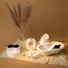 A collection of white baby bath and potty training accessories arranged on a light-colored cloth against a plain brown background. Produktbild-Vorschau
