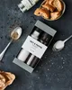 A salt and pepper grinder set is presented in a gift box, surrounded by scattered peppercorns, a spoon of ground pepper, a spoon of salt, and some bread slices in a bowl. Produktbild-Vorschau