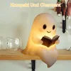 A cute ghost lamp is sitting on a shelf and reading a book, with two glasses next to it. Produktbild-Vorschau