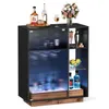 A black bar cabinet with fluted glass doors and LED lighting, displaying bottles of alcohol, glasses, and fruit. Produktbild-Vorschau