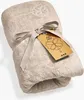A folded beige towel with a ribbon and a tag. Produktbild-Vorschau