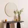 A round mirror with a gold frame hangs above a dark console table with decorative items. Produktbild-Vorschau