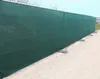 A long, dark green privacy screen fence attached to a metal frame, supported by concrete blocks on a gravel surface. Produktbild-Vorschau