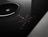 A close-up view of a black induction cooktop with integrated ventilation, showing the digital controls and fan. Náhled obrázku produktu