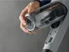 A hand is holding a clear dustbin from a vacuum cleaner. Produktbild-Vorschau