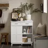 A white cabinet with drawers and shelves is shown in a hallway or entryway setting, styled with decorative items and next to a bench and stool. Produktbild-Vorschau