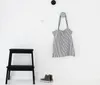 A minimalist interior scene with a black step stool, a striped tote bag hanging on a hook, and a pair of sneakers on the floor. Produktbild-Vorschau