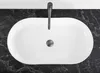 A top-down view of a white oval basin sink with a chrome faucet and drain, set against a black marble countertop. Produktbild-Vorschau