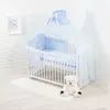 A baby crib with bedding and a teddy bear in a room with white brick walls. Voir les images du produit