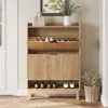 A wooden shoe cabinet with two flip drawers and a lower shelf, filled with shoes and decorated with a handbag and a vase with plants. Podgląd zdjęcia produktu