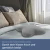 A grey butterfly-shaped pillow is placed on a bed with other pillows and curtains in the background. Produktbild-Vorschau