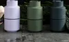 Three spice grinders in different colors are arranged on a textured surface with some greenery in the background. Produktbild-Vorschau