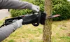 Hands wearing gloves operating an electric chainsaw to cut a tree trunk outdoors. Produktbild-Vorschau