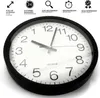 A close-up, slightly angled view of a black-framed wall clock with a white face and black numbers. The clock is shown from a diagonal perspective, with the top-left portion of the clock face most prominent. Several icons and text descriptions are present a Podgląd zdjęcia produktu