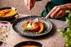A person is eating a dessert made from pumpkin, served with ice cream, on a plate. There is also a bowl of soup in the background. Náhľad obrázku produktu