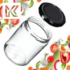A clear glass jar with a black lid is shown, surrounded by various fresh vegetables and herbs, suggesting a context of preserving or preparing food. A stylized 'K' logo is also visible. Podgląd zdjęcia produktu