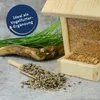 A wooden bird feeder filled with birdseed, with a scoop of birdseed in the foreground and some decorative grass and a piece of wood. Produktbild-Vorschau