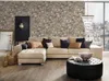 A living room scene with a sectional sofa, ottoman, and decorative items, featuring a stone-patterned wallpaper. Produktbild-Vorschau