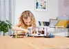 A young girl playing with a toy camper van set on a wooden table. Voir les images du produit