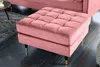 A pink velvet ottoman with tufted top and gold-tipped black legs sits on a dark floor next to a grey rug. Produktbild-Vorschau
