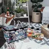 A picnic setup on a balcony with a cooler bag, food platter, drinks, and plants. Náhled obrázku produktu