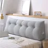 A bed with a large grey wedge pillow against the headboard, with decorative items on a shelf above. Produktbild-Vorschau