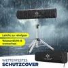 A black protective cover for a heater is shown on a silver tripod stand, with rain falling in the background. Produktbild-Vorschau